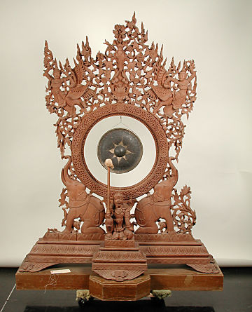 A carved wood stand with a gong in the center. It features an elephant on each side of the central figure holding the mallet.