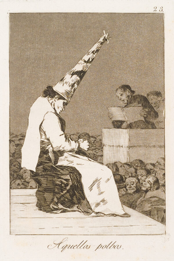 A man judges another, who sits wearing an inquisition pointed hat, before a crowd.