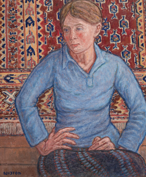 A woman in a blue shirt in front of a woven tapestry.