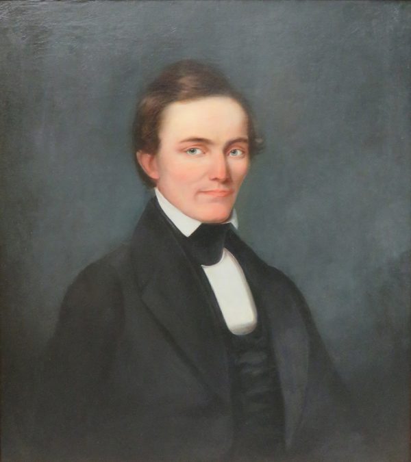 Portrait of a man wearing a white shirt and black coat and tie.