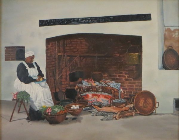 A southern mammy wearing black shirt and white dress and hat, sits to the left of a large fireplace.