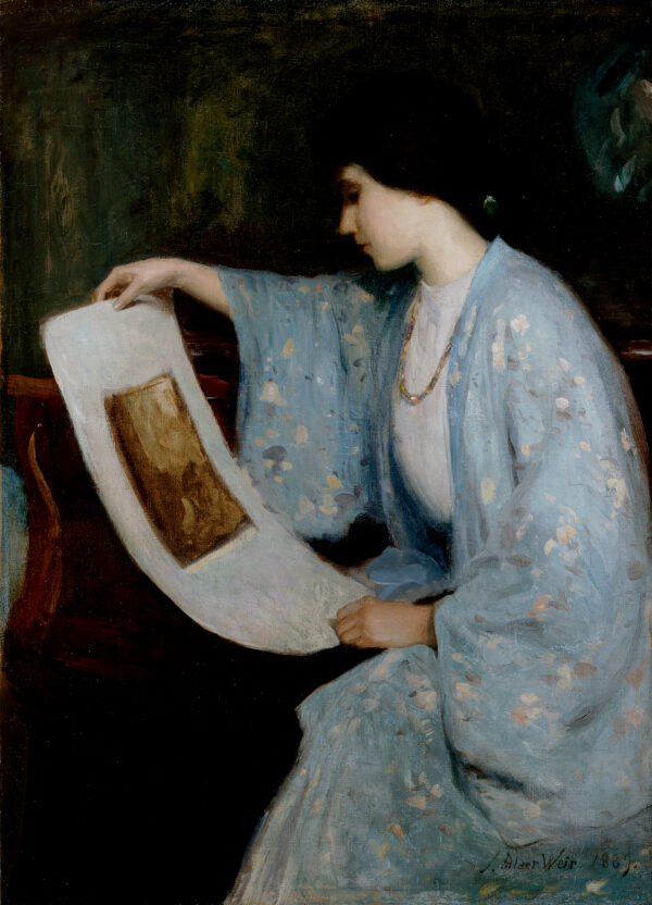 A woman in a blue kimono sits, leaning to her right, looking at a large print in her hands.