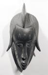 Elongated head; crested hair piece; small, slanted, oval eyes; elongated nose; carved facial scars on cheeks and forehead.