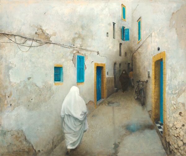 A woman covered in white with high heels moves down a narrow street with blue doors and windows. Essaouira in on the Moroccan coast.