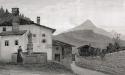 A house with a woman standing in front of a well and statue.