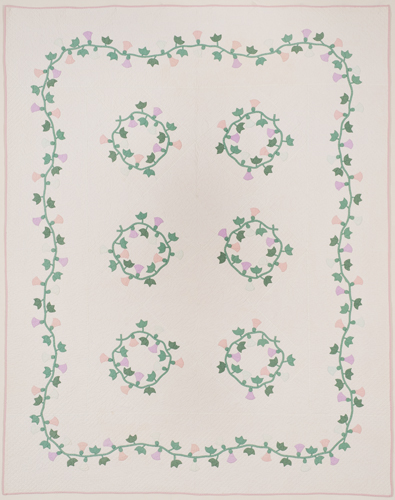 Appliqued floral pattern in pink, lavender & green on quilted white ground. Backing in solid pink. The floral pattern consists of nine flower wreaths in center and a flowereing vine border. The blossoms of both the wreaths & vine resemble the 