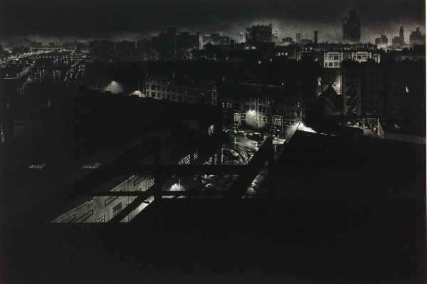 Bird's eye view of cityscape at night.  In foreground, view from above through girders to street below.  In middle ground, partial view of street scene with parked cars and tenement buildings.  In distance, view of city buildings along skyline.  At upper left corner, jewel-like arrangement of street & automobile lights.