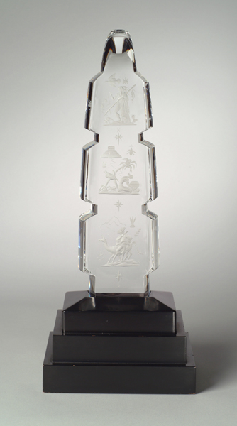 A Steuben crystal exhibition piece # x3267. Blank designed by Lloyd Atkins in 1959, Bruce Moore designed the drawings of three scenes from early America. The three segmented glass sits on a black tiered illuminated base.