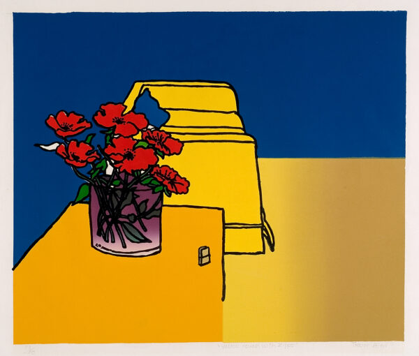 Red flowers in a vase on a table in front of a yellow couch with blue background.