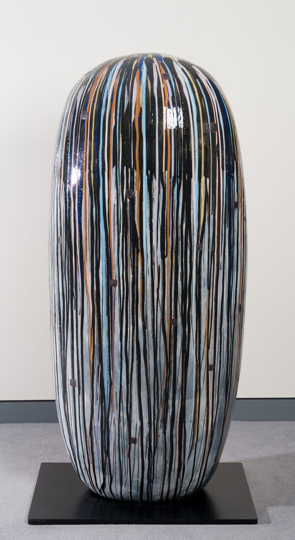 Flattened column with rounded top. The surface is multicolored vertical drips of glaze on a cream background. There are black on rust colored squares scattered throughout.