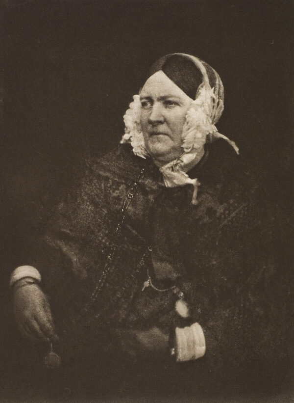 Portrait of a seated woman. She has a head covering with white flowers at each side of her head. Her right hand holds a watch that is on a beaded chain around her neck.