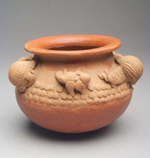 Bowl is a buff body with terra cotta wash inside and at rim and bottom of bowl. A band of animal sculpture rims the shoulder. There are 3 large, 3 small figures on a background of round 1/4