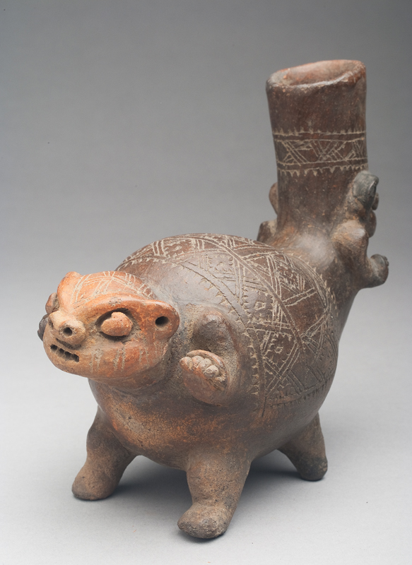 The vessel is dark brown with red ochre on one face. One end has an animal head, arms and feet, the other end seems more human with the spout of the vessel formed from his head. There are geometric incised marks on the body.