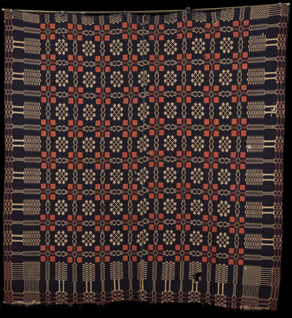 A double weave coverlet in blue/black, rust and cream colors. The coverlet is made in such a way that the reverse side of the coverlet is a mirror image of the front.