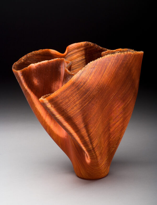 The vessel was made by fusing threads of orange glass together then folding the sides into a distinctive shape.