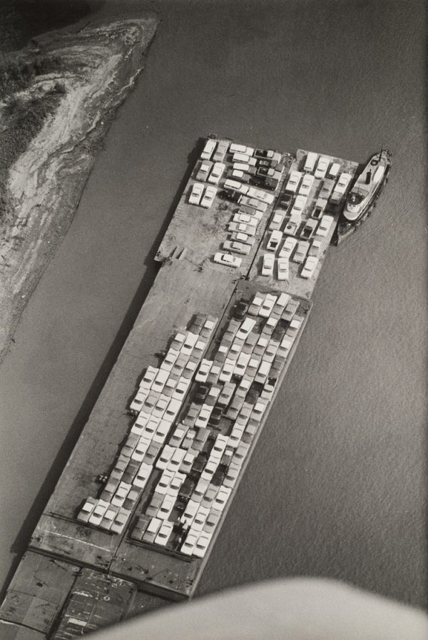 New cars are lined up on a barge in the Mississippi river. The plane’s wing is visible at bottom.