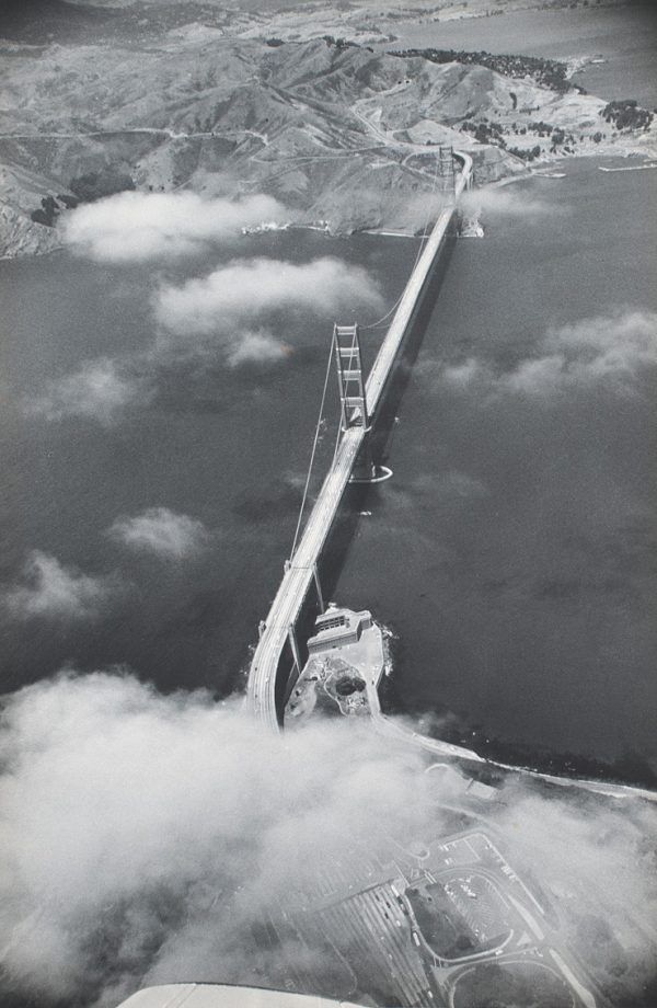 The Golden Gate bridge running from lower left to upper right. The bottom is full of clouds and just the tip of the plane wing shows.