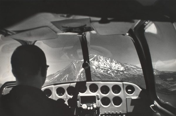 View of cockpit with pilot and Mount Shasta through windshield.