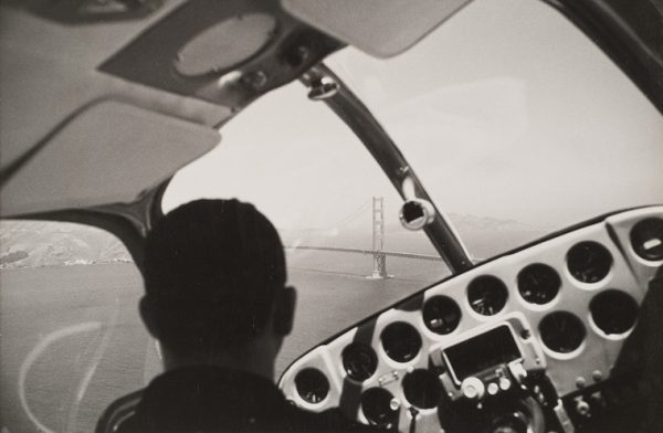 View of cockpit with pilot and Golden Gate bridge through windshield.