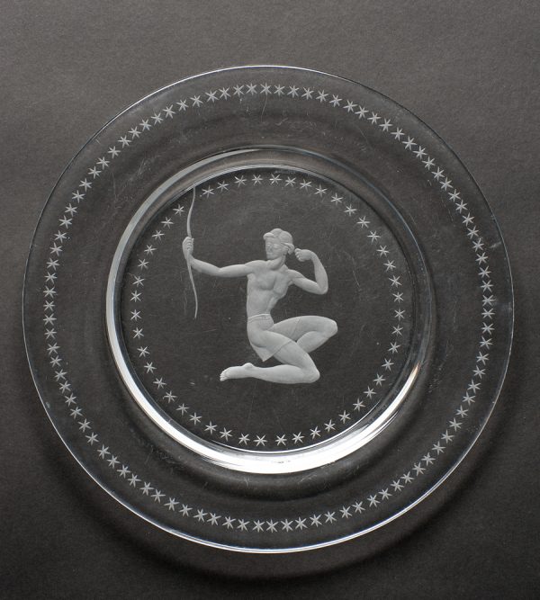 A plate with the image of a crouching man pulling a bow with no strings. Stars surround the image as well as the outer rim.