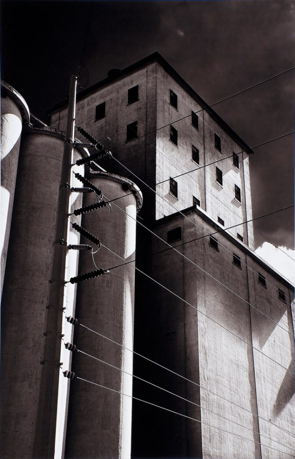 Vertical image of grain elevators with power lines.