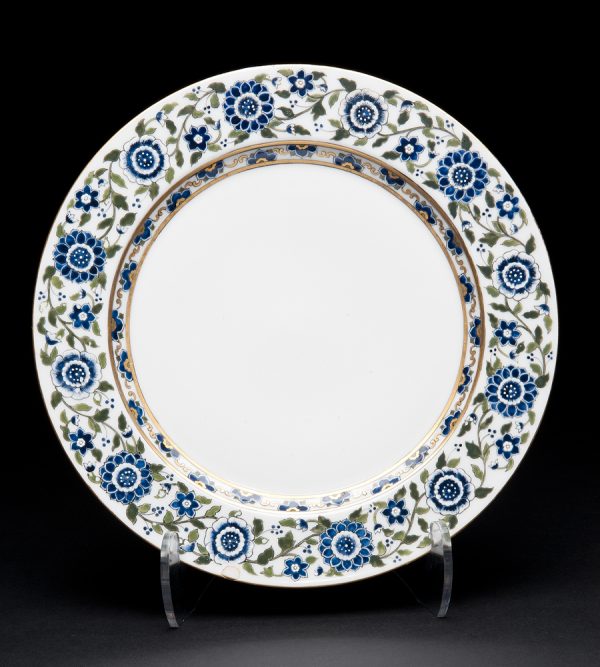 White plate with blue and white flowers and green foliage, gold accents.