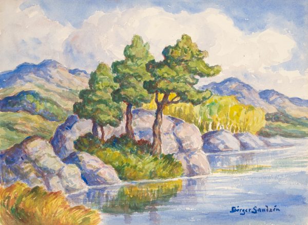 Three trees stand surrounded by large rocks on the edge of a body of water.