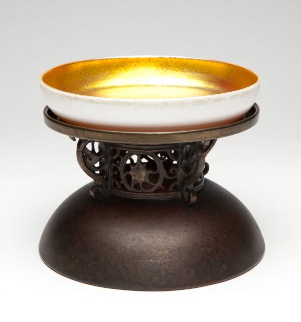 A bronze compote with gold Aurene on Calcite bowl by Steuben. The compote has a large foot with open design of grapes in the stem separated by four bird’s head flanges.