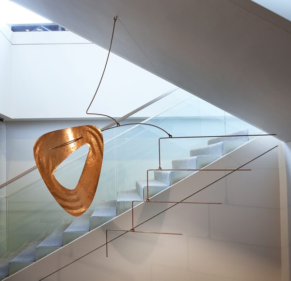An abstract hanging mobile of a flat oblong disk on the left with four L-shaped rods on the right.
