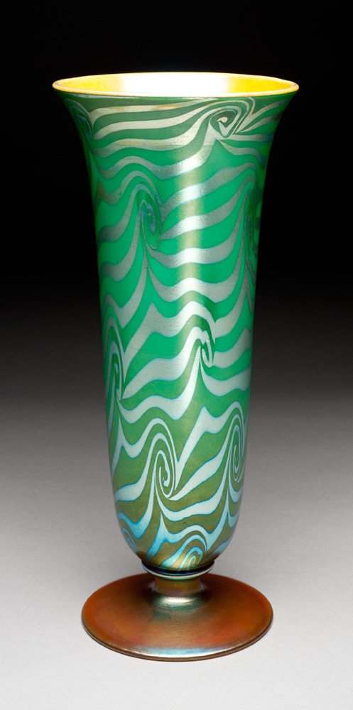 A tall vase with green background, silver King Tut design, gold iridescent foot, butterscotch interior.