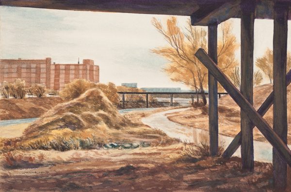 A mid-fall landscape with a large wooden platform above. To the right of the platform supports is a sidewalk that curves toward the center then back to the right around a small hill. A pile of rock or debris is at lower left. Across the river are two pinkiish-red brick buildings on the left. Scene is in Wichita.