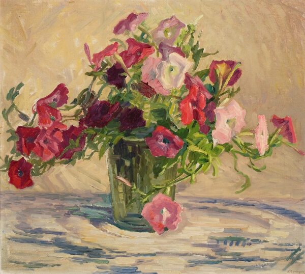 A bouquet of pink and red flowers in a glass vase on a white with blue tablecloth.
