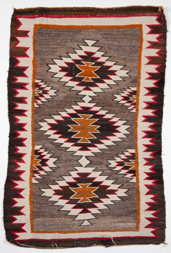 A rug in brown, cream, orange and red colors. There are three main diamond patterns with two smaller on each side and two along the long sides.