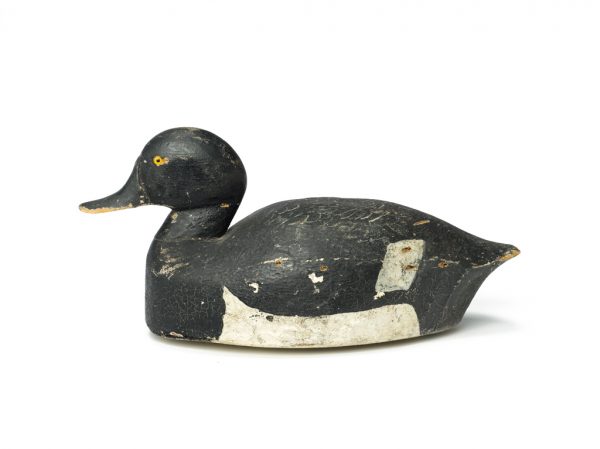 A painted wood decoy, black with white belly and wingtips.