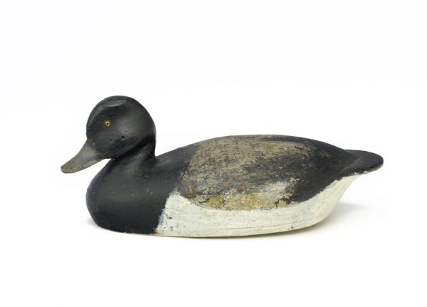 A black duck decoy with white bottom, grey wing, swirls on top. It has yellow and black eyes.