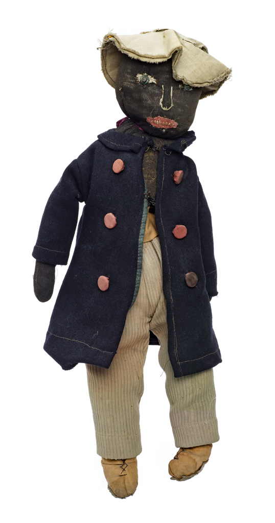 Male doll with tan fabric hat. His coat is black with faded orange buttons. He wears tan ribbed pants. The fill is pea sized organic matter (straw, sticks and seeds). The eyes are fabric colored beads, the mouth is appliquйd and embroidered. He wears a red ribbon around his neck.
Made by same maker as 2016.1.9