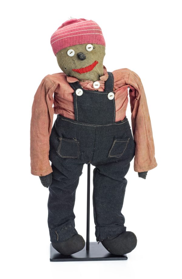 A male doll in black overalls, pink shirt and knit stocking hat. The mouth is embroidered, and the same buttons used on the shirt and overalls are used for the eyes. The nose is a fabric that is folded over.