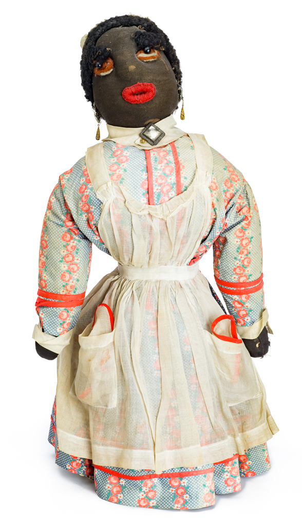 A female bottle doll wears a blue with white and pink flowered dress. The dress has a white collar with a square stone at the neck center. The white apron is full with two pockets including handkerchiefs.