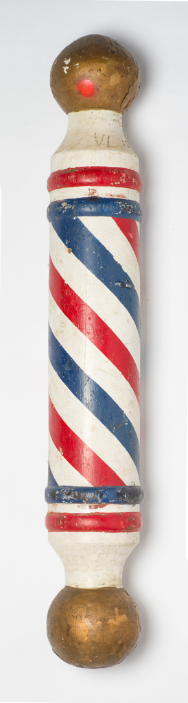 A turned wood barber pole with a round knob on either end. The pole was painted overall with gold end knobs and a red, white, and blue striped body.
