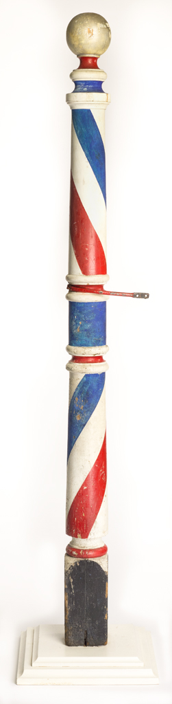 A tall barber pole on a a square, stepped pedestal base. The pole is made of turned and painted wood. It has a black square base, red white and blue striped motif, and silvery spherical finial at the top. There is a painted iron-alloy bracket at the midpoint that would be used to secure the post to a support. The tiered base may be a later addition to the piece.