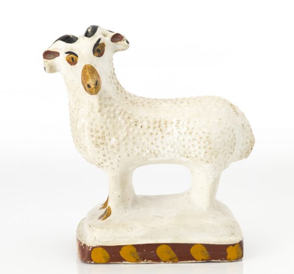 A mold made chalk ware figure of a white ram with painted facial features and border around the base.