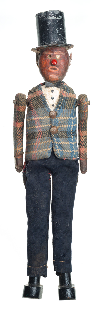 A male doll made of carved and painted wood. The doll is wearing a plaid coat with tails, dress pants, a top hat and bow tie. The bow tie and hat are made from painted galvanized sheet metal.