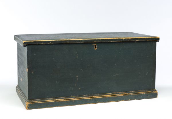 .A plain chest with hinged lid. The outside is dark green and the interior is unpainted light wood. At top center is a lock.
