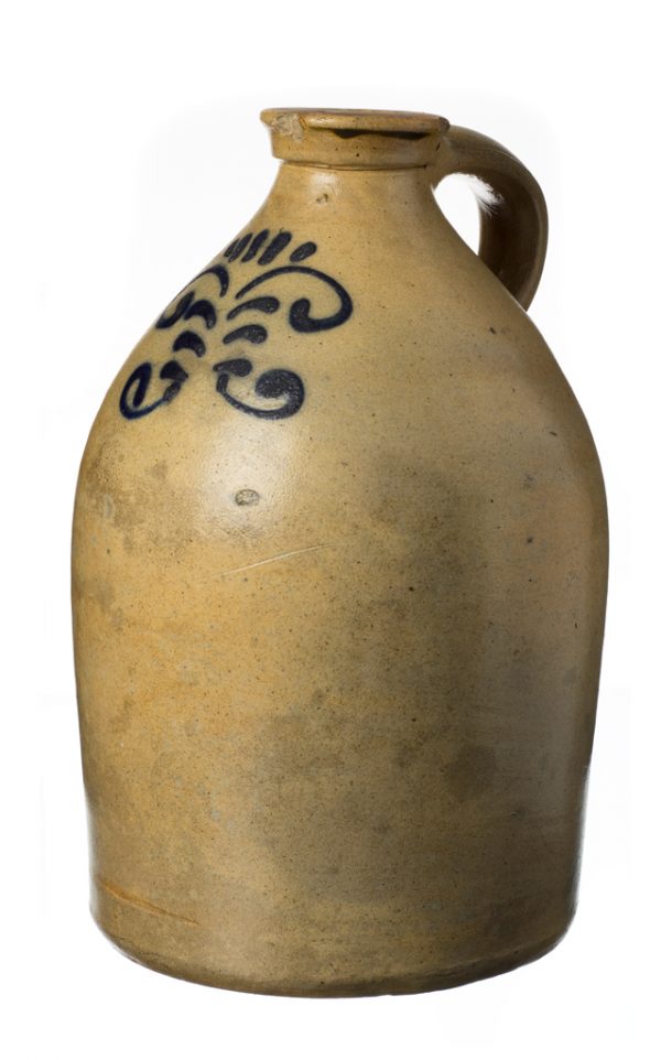 A glazed stoneware jug with one handle and a flat mouth. There is a cobalt blue pattern on one side.