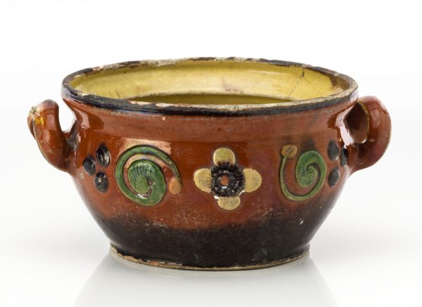 The bean pot does not have a cover. A glazed stoneware dish with two handles. The interior has a pale yellow glaze, while the exterior has a red-brown glaze with raised floral ornaments.