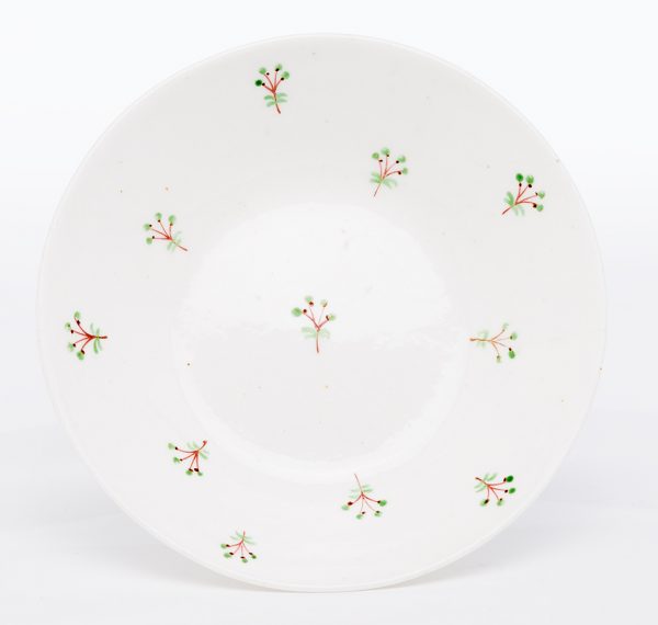 A small ceramic saucer with clear speckled high-gloss glaze and sprig pattern overglaze. The
ceramic body is white and translucent, likely porcelain.