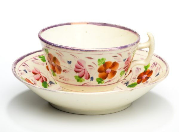 A cup and saucer set of red and pink flowers, green leaves on cream background.