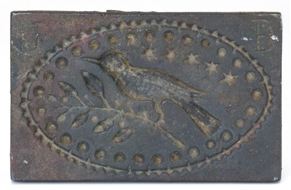A cast iron cookie or butter press of a bird on a twig surounded by stars within an oval.