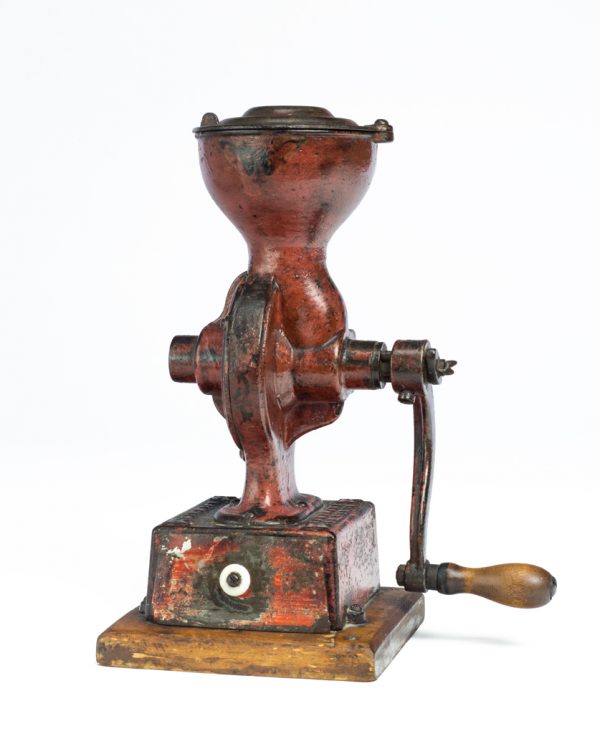 An hour glass shaped coffee grinder with a single handle and drawer to catch the grounds. Red painted mill with thin metal tray, white knob, wood handle.
