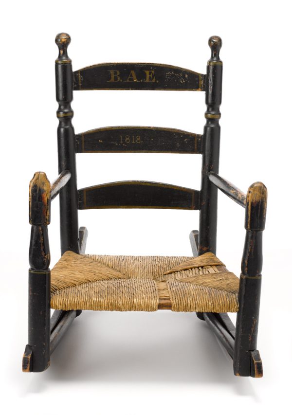 Black painted ladder-back child's arm chair, with added rockers. The back has in gold letters “BAE” and 